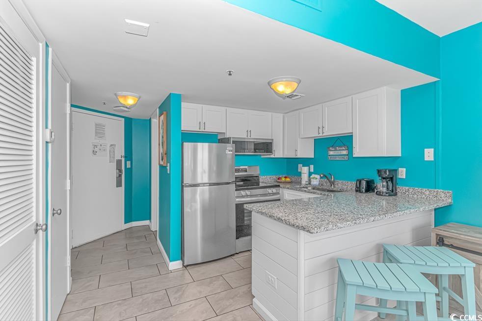 1605 South Ocean Boulevard, Unit 705 Myrtle Beach, SC 29577 - Photo 33 of 38 Kitchen featuring stainless steel appliances, a peninsula, white cabinets, light stone countertops, and a breakfast bar