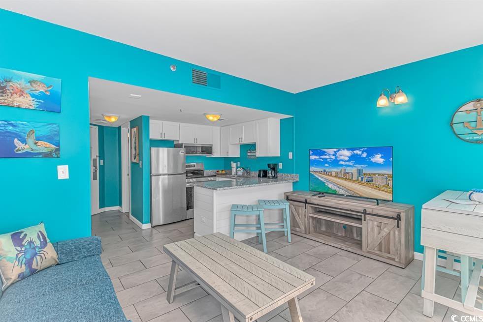 1605 South Ocean Boulevard, Unit 705 Myrtle Beach, SC 29577 - Photo 8 of 38 Kitchen featuring white cabinetry, appliances with stainless steel finishes, light stone counters, a breakfast bar area, and a peninsula