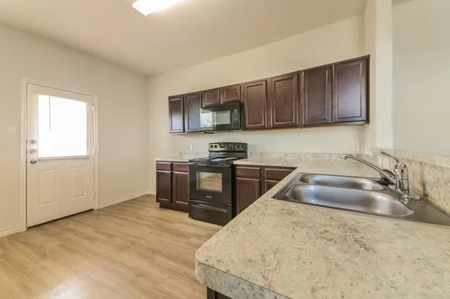 a kitchen with granite countertop a stove a sink and a microwave oven with wooden cabinets