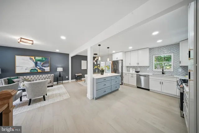 a large white kitchen with lots of counter space a sink wooden cabinets and view living room