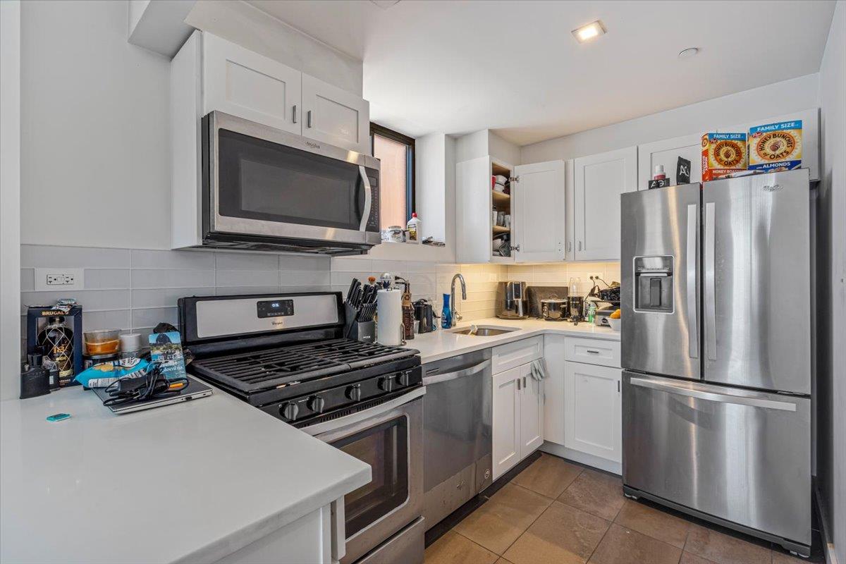 87-22 51st Avenue, Unit 4H Queens, NY 11373 - Photo 6 of 17 Kitchen with tasteful backsplash, light countertops, white cabinetry, stainless steel appliances, and a sink