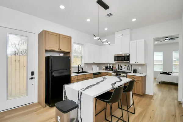 a kitchen with stainless steel appliances kitchen island granite countertop a refrigerator a stove a sink a dining table and chairs with wooden floor