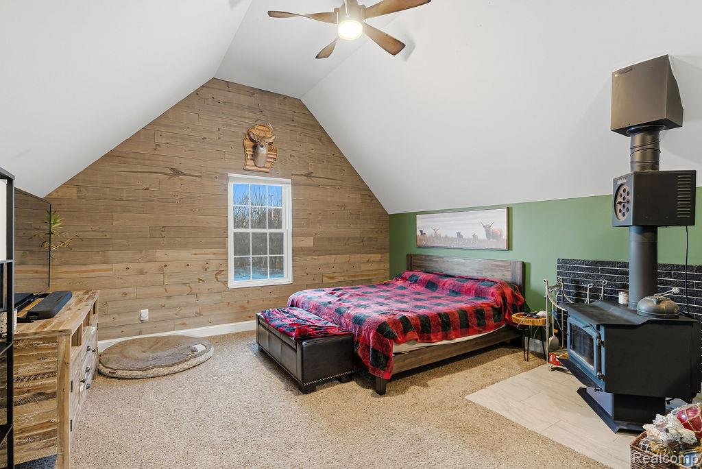5216 South State Road Goodrich, MI 48438 - Photo 24 of 52 Bedroom featuring wooden walls, a wood stove, carpet, a ceiling fan, and vaulted ceiling