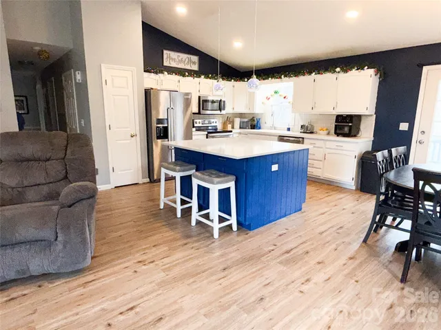 a kitchen with stainless steel appliances granite countertop a refrigerator a sink dishwasher a stove and a dining table with wooden floor