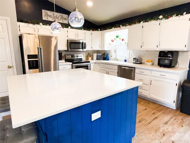 a kitchen with granite countertop a refrigerator a stove a sink dishwasher and white cabinets with wooden floor