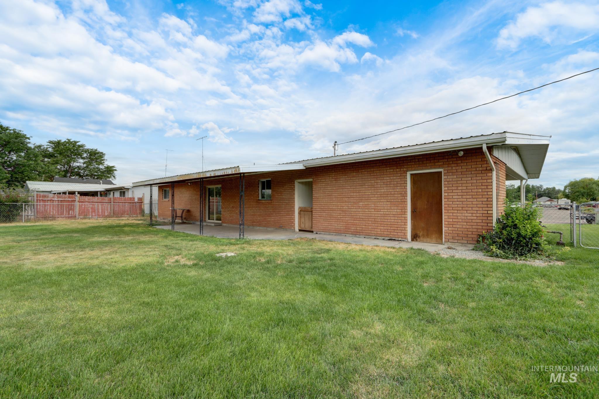 801 Thompson Avenue Nyssa, OR 97913 - Photo 38 of 46 Expansive green space featuring a brick exterior, covered patio, sliding glass door access, and a chain-link fence