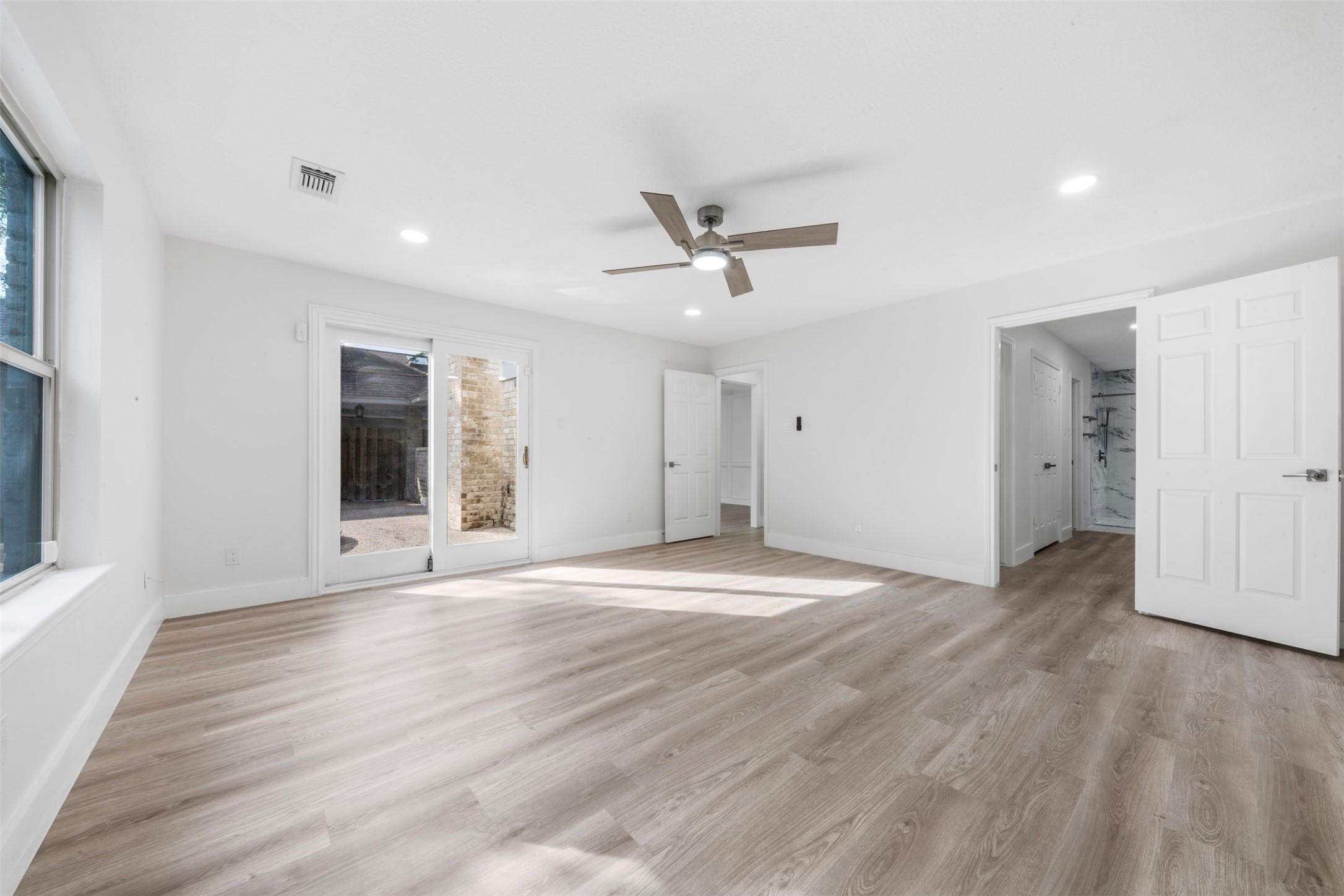 9543 Enstone Circle Spring, TX 77379 - Photo 18 of 50 This bright, spacious room features wood-style flooring, a ceiling fan, and ample natural light from large windows. It includes sliding glass doors leading outside and an attached bathroom with modern finishes.
