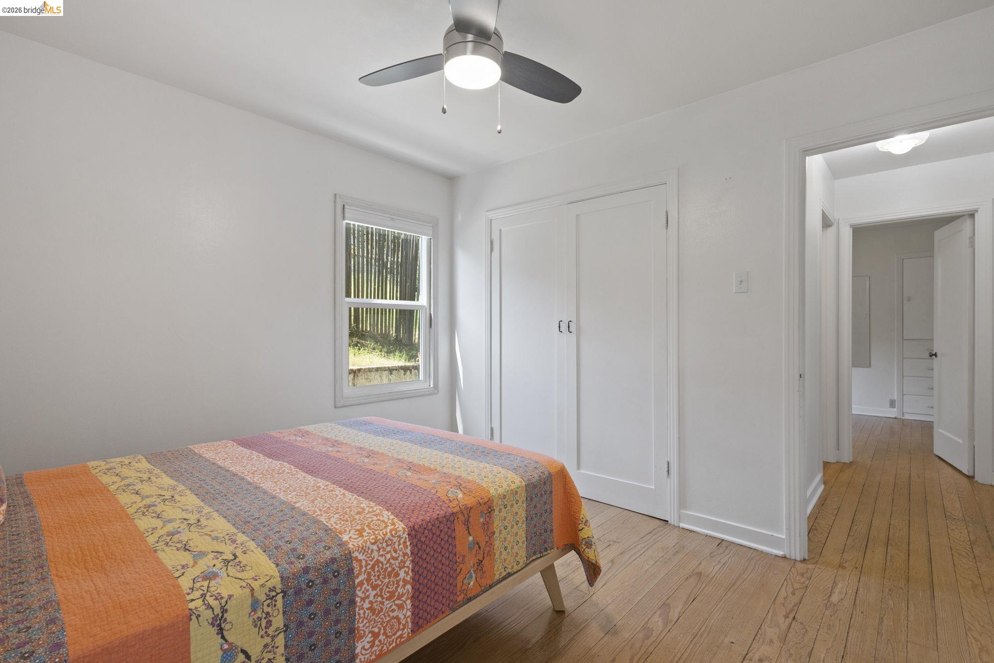 18363 Yosemite Road Tuolumne, CA 95379 - Photo 11 of 34 Room featuring wood-finish flooring, a double-door closet, a window with exterior scenery, a ceiling fan with integrated lighting, and white walls