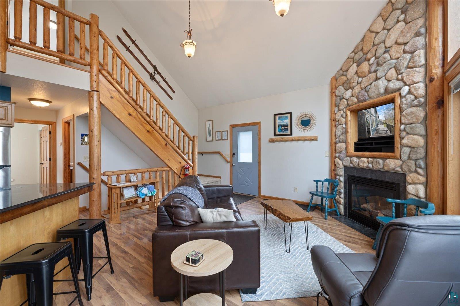 6266 Giants Ridge Road Biwabik, MN 55705 - Photo 11 of 37 Open-concept living area featuring a stone fireplace with a dark surround, wood-finish flooring, and a natural wood staircase with log railings