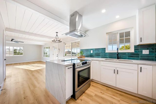 a kitchen with granite countertop a stove a sink and white cabinets with wooden floor