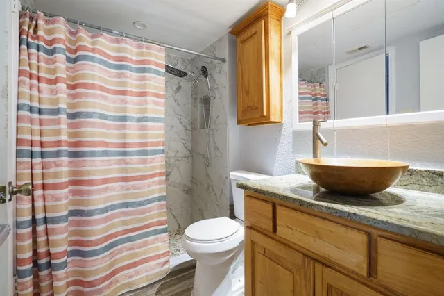 a bathroom with a granite countertop sink a toilet a mirror and shower curtain
