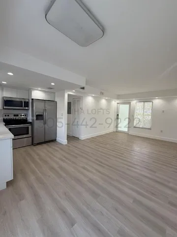 a view of an empty room with kitchen and window