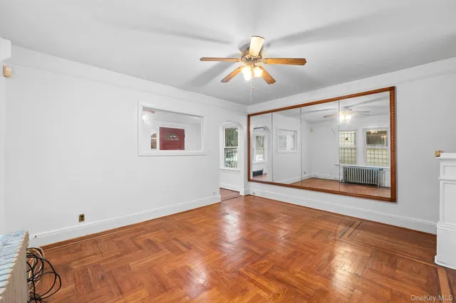 a view of an empty room with wooden floor and a ceiling fan