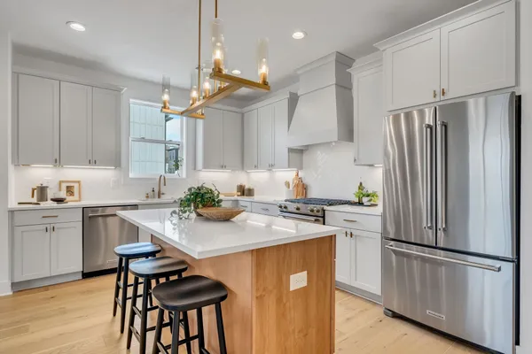 a kitchen with stainless steel appliances granite countertop a refrigerator a sink dishwasher a stove and white countertops with wooden floor