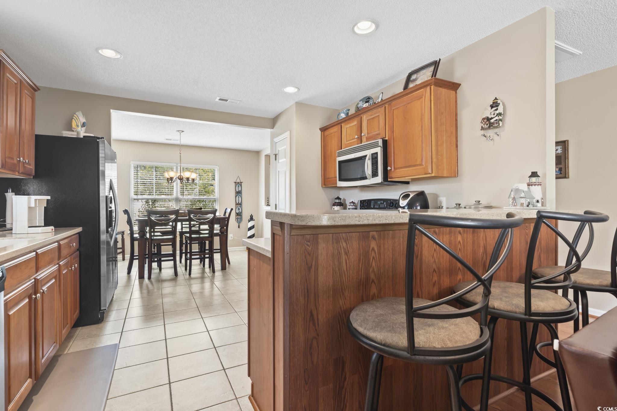 2288 Beauclair Court Myrtle Beach, SC 29579 - Photo 12 of 40 Kitchen featuring light tile patterned floors, brown cabinetry, stainless steel microwave, a peninsula, and a notable chandelier