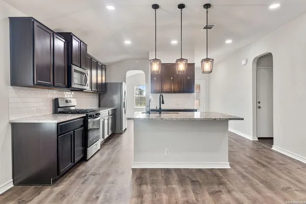 a kitchen with stainless steel appliances granite countertop a sink a stove and a wooden floors