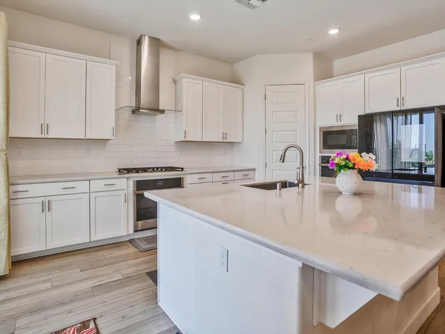 a kitchen with stainless steel appliances granite countertop a sink stove and white cabinets with wooden floor