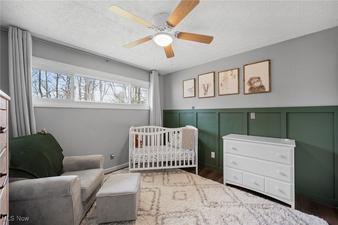 87 Kenridge Road Akron, OH 44333 - Photo 35 of 48 Bedroom featuring a ceiling fan, wainscoting, a textured ceiling, wood finished floors, and a nursery area