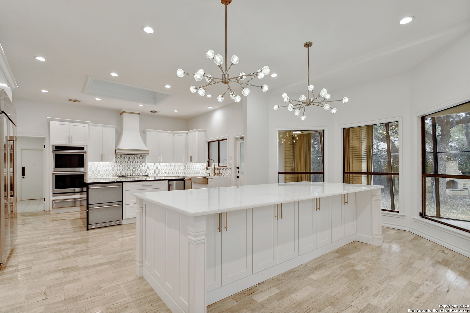a large white kitchen with kitchen island a chandelier and living room view