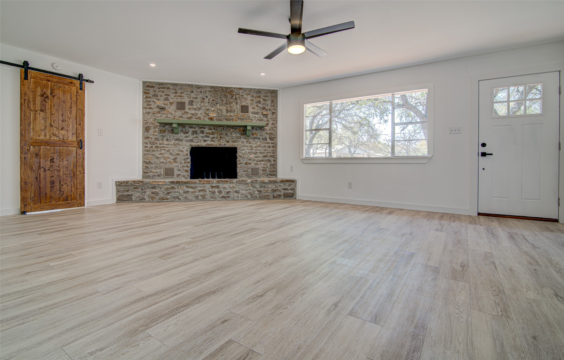 207 Haley Road Johnson City, TX 78636 - Photo 8 of 31 A spacious living room features a striking stone fireplace, wide plank flooring, and a modern ceiling fan.
