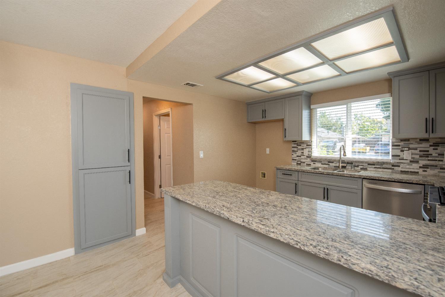 1621 Davis Street Ripon, CA 95366 - Photo 11 of 43 kitchen with gray cabinets, light stone countertops, tasteful backsplash, dishwasher, and light wood-style flooring