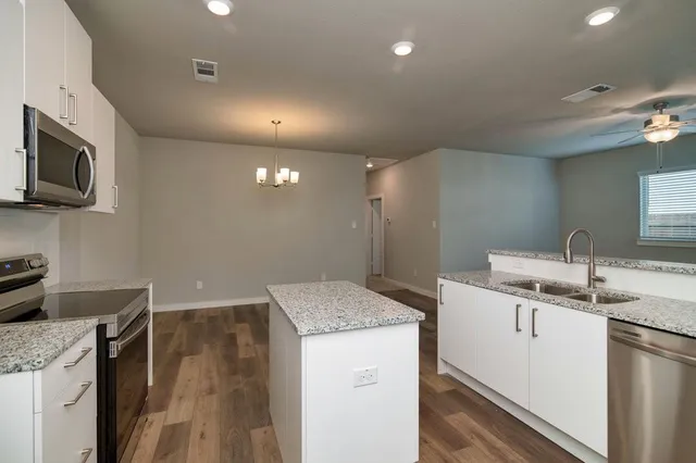a kitchen that has a sink a microwave oven a stove and white cabinets with wooden floor