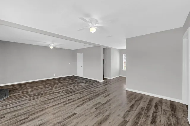 a view of an empty room with wooden floor and a ceiling fan