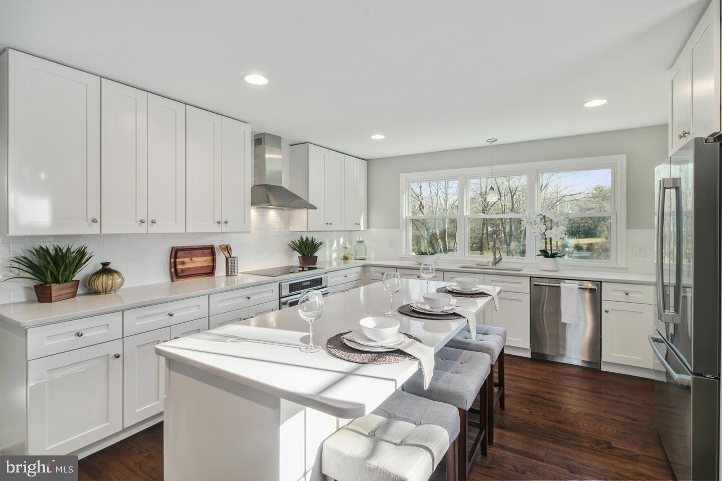 a open dining room with stainless steel appliances kitchen island granite countertop a refrigerator a stove a sink dishwasher and white cabinets with wooden floor