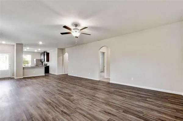 a view of an empty room with wooden floor and a ceiling fan