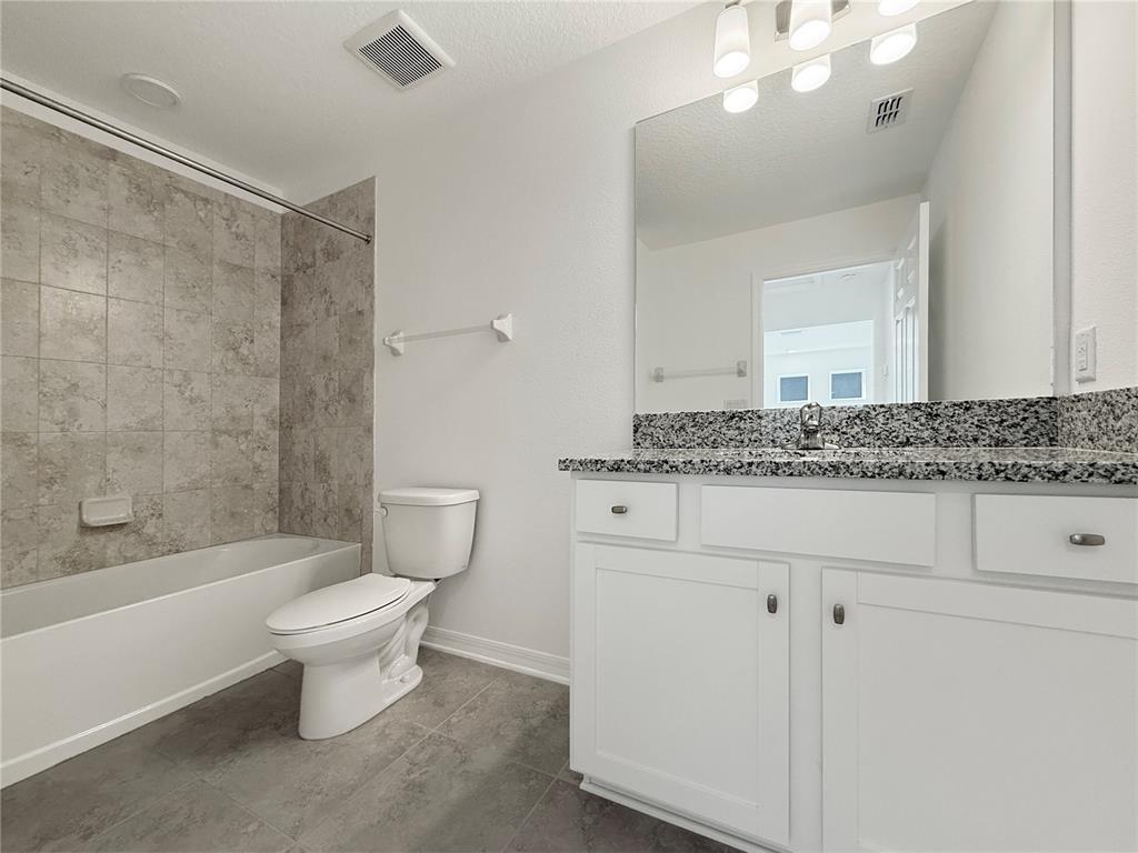 3023 Adams Cross Drive Zephyrhills, FL 33540 - Photo 12 of 36 a bathroom with a granite countertop toilet a sink a mirror and bathtub