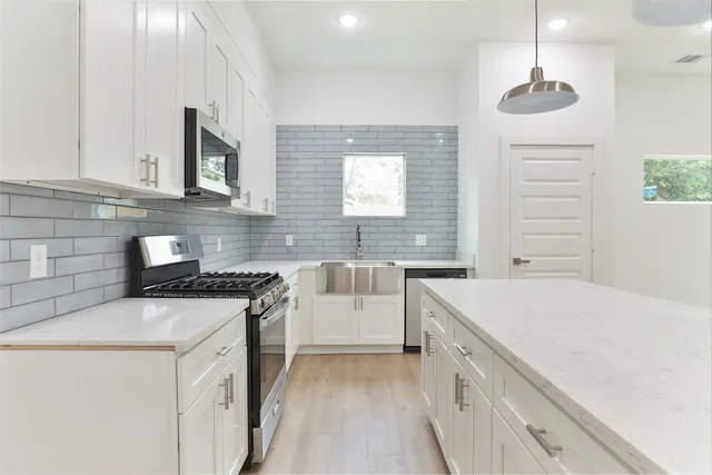 a kitchen with stainless steel appliances granite countertop a sink a stove a refrigerator and white cabinets with wooden floor