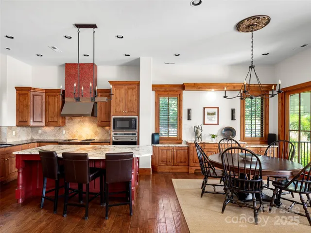 a open kitchen with stainless steel appliances granite countertop a dining table chairs and white cabinets