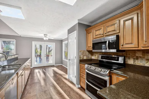 a kitchen with stainless steel appliances granite countertop a stove top oven a sink dishwasher a dining table and chairs with wooden floor