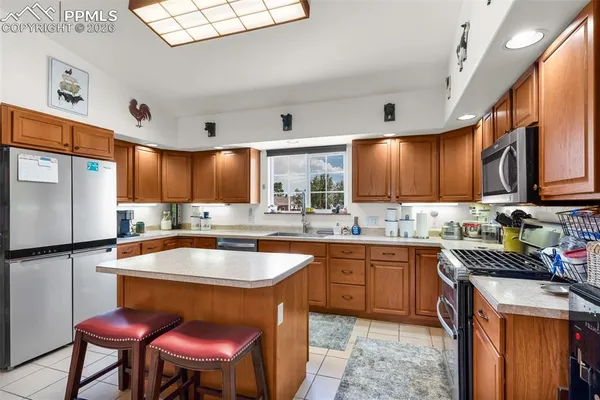 a kitchen with stainless steel appliances granite countertop a sink a stove a refrigerator cabinets and chairs