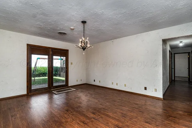 an empty room with wooden floor chandelier and windows