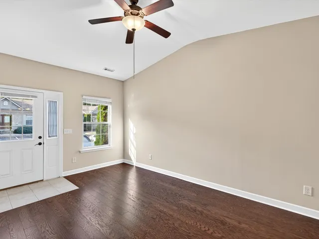 an empty room with wooden floor fan and windows