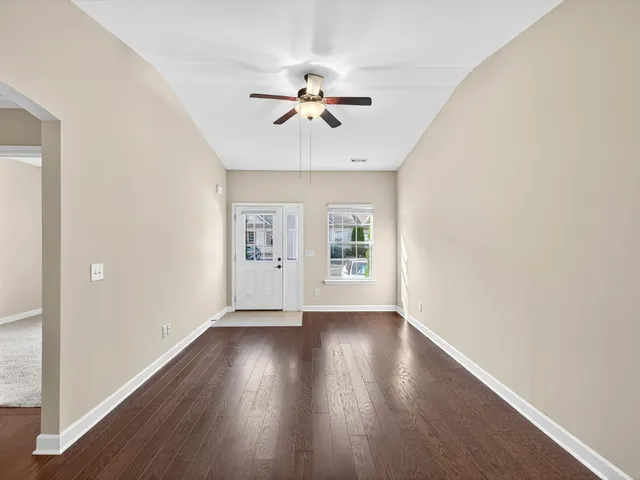 an empty room with wooden floor chandelier fan and windows