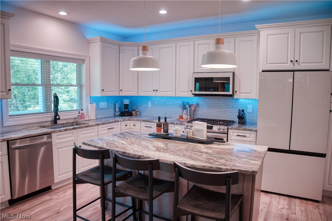 4553 Sharon Copley Road Medina, OH 44256 - Photo 2 of 32 Kitchen featuring white shaker cabinetry, stainless steel appliances, a center island with seating, a mosaic tile backsplash, and light wood-finish flooring