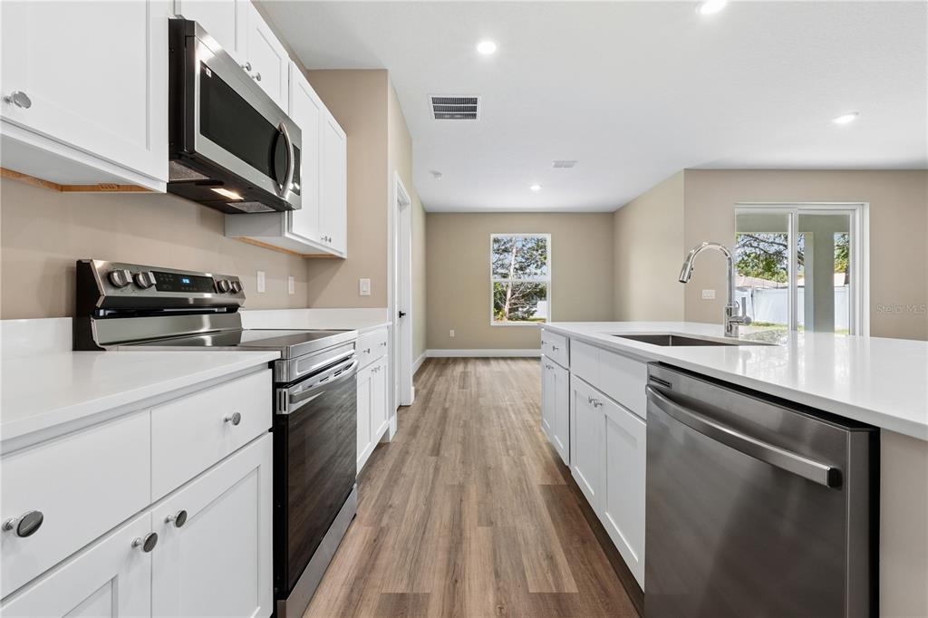 21 Postman Lane Palm Coast, FL 32164 - Photo 2 of 13 a kitchen with stainless steel appliances granite countertop a sink a stove top oven a chimney wooden floor and cabinets