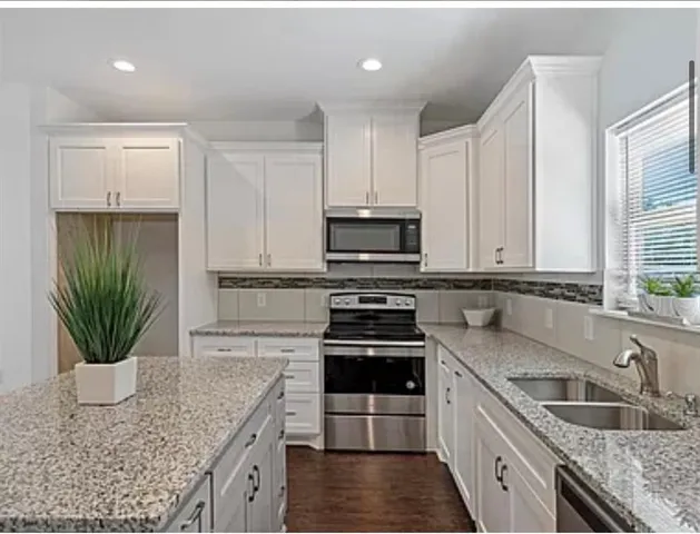 a kitchen with granite countertop a sink stainless steel appliances and furniture
