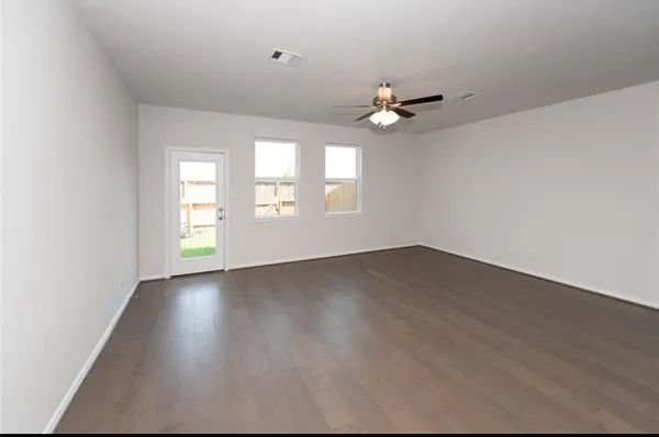 an empty room with wooden floor chandelier fan and windows