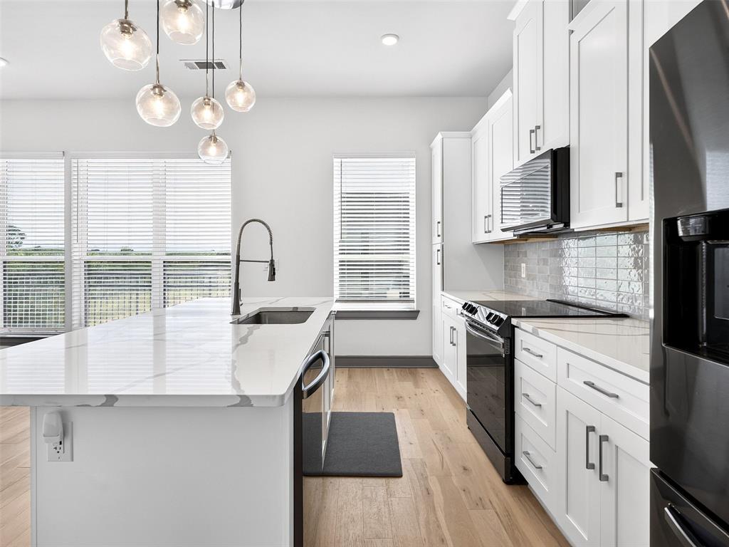 2700 Old Denton Road, Unit 2212 Carrollton, TX 75007 - Photo 16 of 38 Kitchen featuring a quartz-finish island with an undermount sink, pendant lighting, wood-finish flooring, white cabinetry, and a tile backsplash
