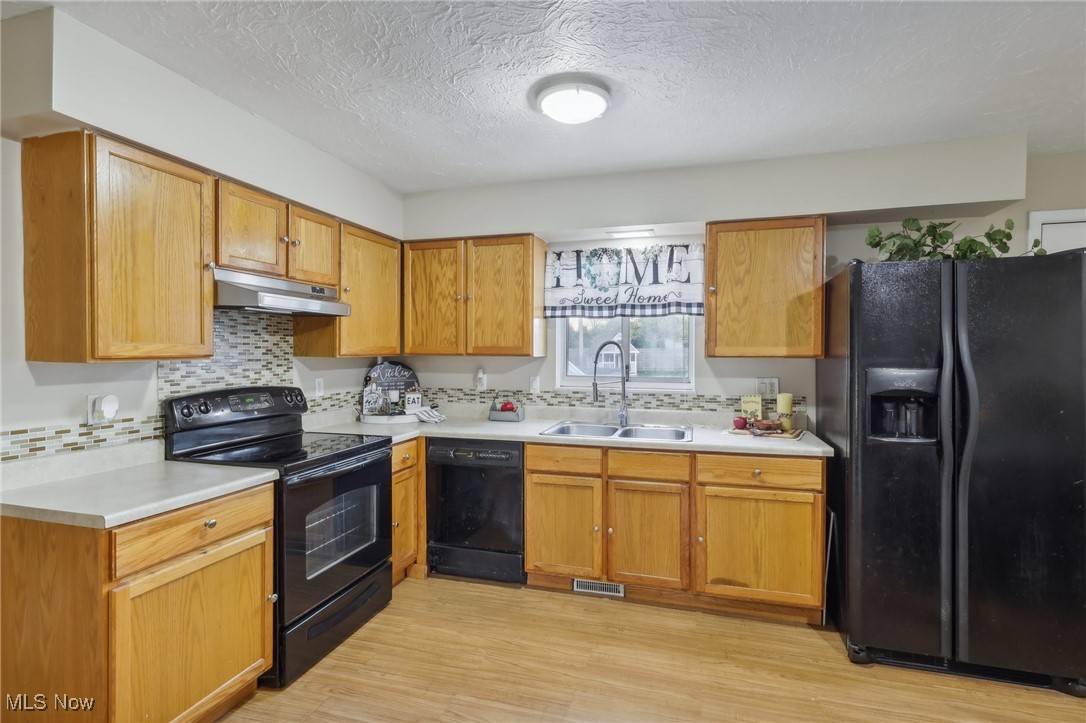 167 Birch Road Painesville, OH 44077 - Photo 9 of 49 Kitchen with black appliances, a textured ceiling, sink, tasteful backsplash, and light hardwood / wood-style flooring