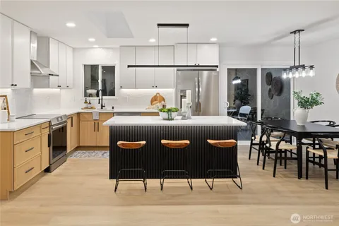 a kitchen with stainless steel appliances granite countertop a sink a stove a refrigerator and chairs