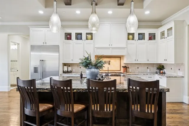 a kitchen with stainless steel appliances kitchen island granite countertop a dining table chairs and a refrigerator