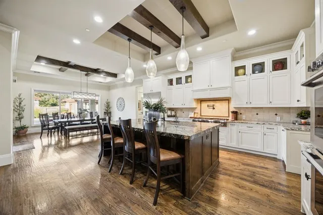 a open kitchen with stainless steel appliances granite countertop a stove top oven a sink a dining table and chairs with wooden floor