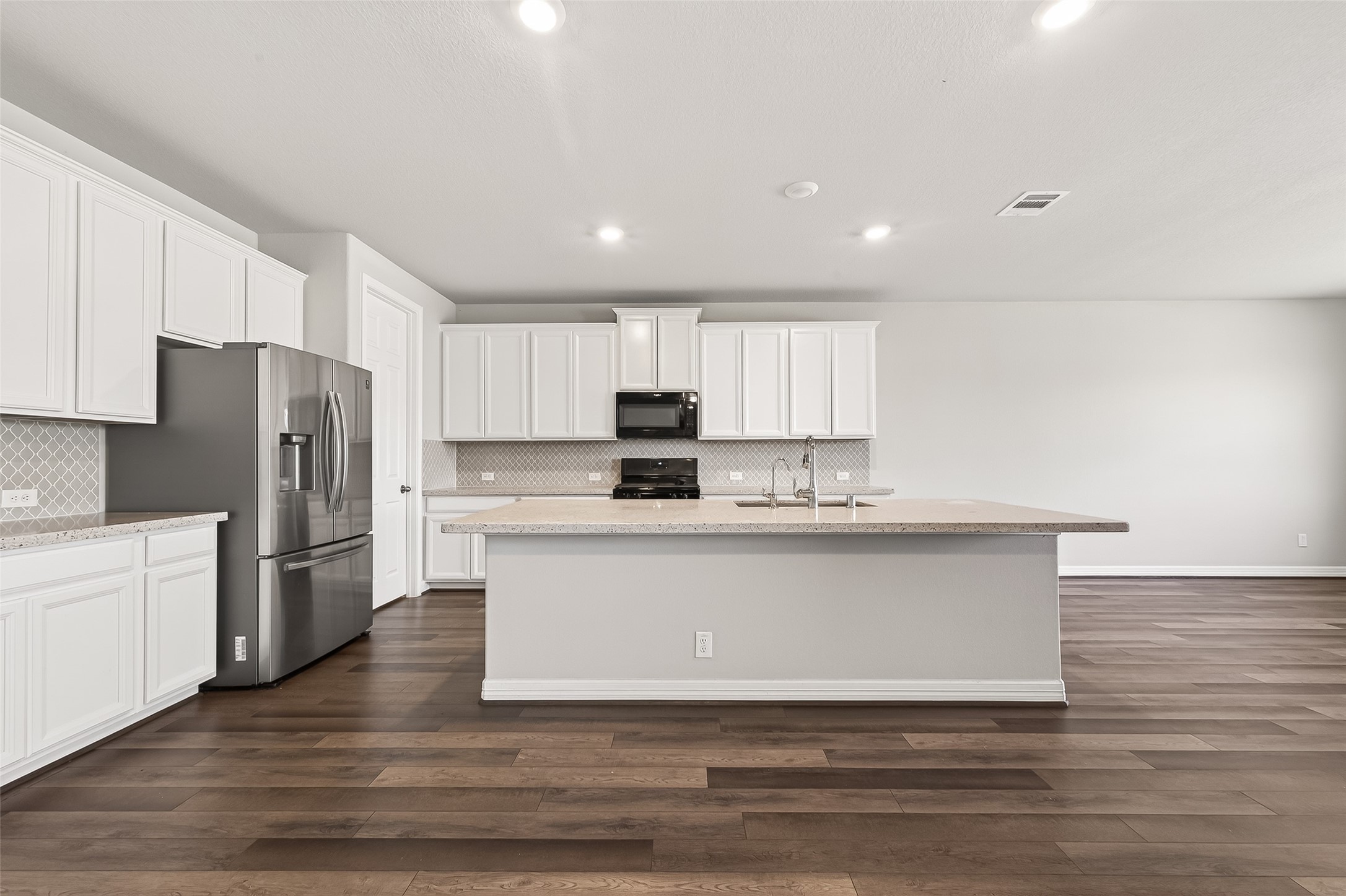 444 Round Lake Drive Rosenberg, TX 77469 - Photo 16 of 50 This stunning gourmet kitchen features a massive, centrally located island topped with luxurious quartz countertops, offering generous seating for guests and effortless entertaining. Sleek white cabinetry provides abundant storage options, complemented by a striking hexagon tile backsplash that adds a modern designer touch. The space is beautifully illuminated with ample recessed lighting and includes a spacious walk-in pantry for exceptional organization and convenience.