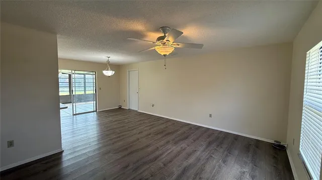 an empty room with wooden floor fan and windows