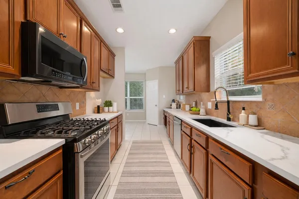 a kitchen with stainless steel appliances a sink dishwasher a stove top oven a refrigerator with wooden cabinets and floor