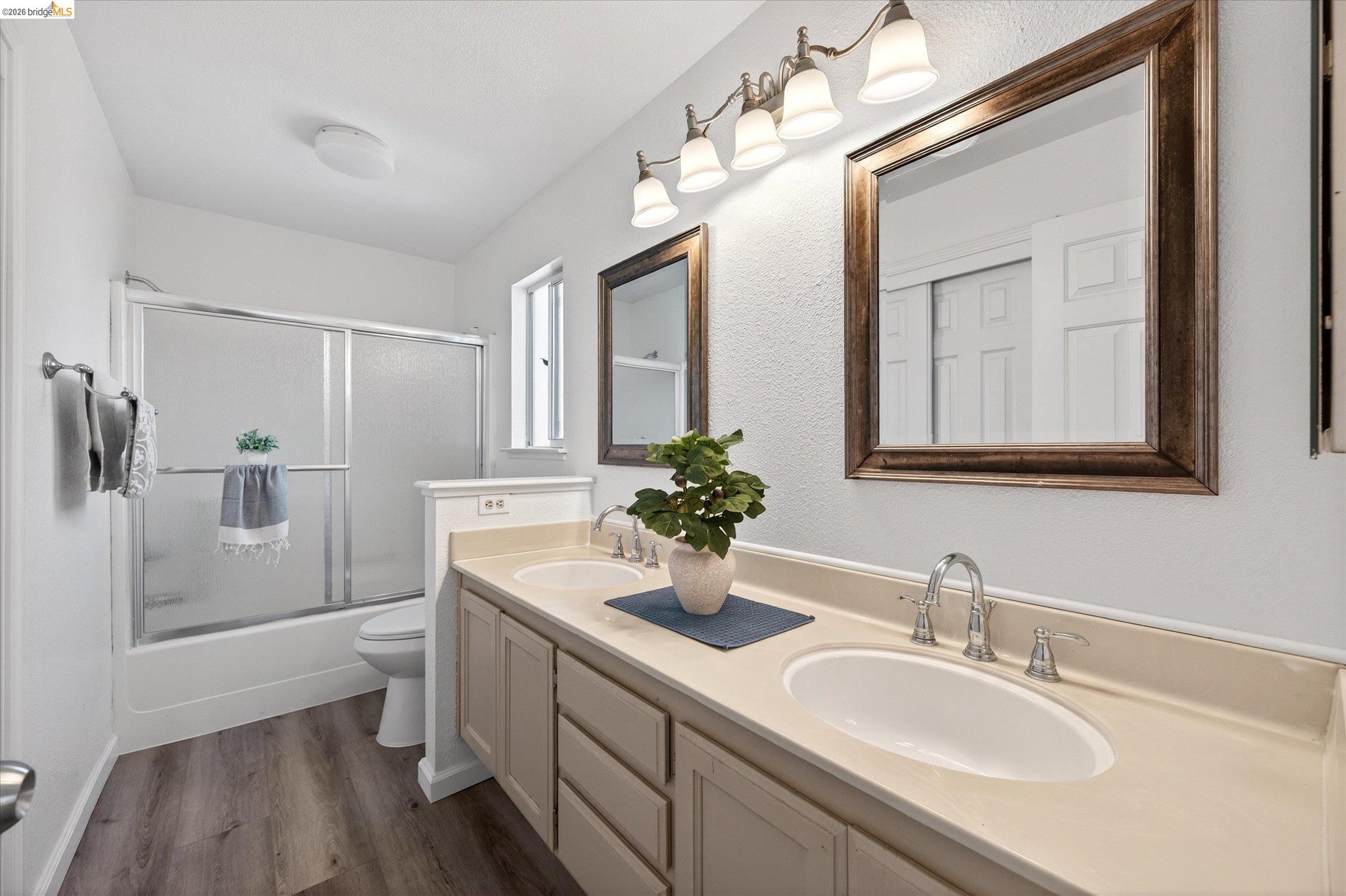 1120 Deerpark Road Oakley, CA 94561 - Photo 21 of 30 Double vanity with integrated sinks and chrome fixtures, framed mirrors, wood-finish flooring, and a bath/shower combination with sliding glass doors